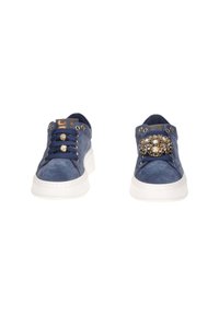 Un paio di sneakers blu scamosciato con suole bianche, lacci navy, occhielli dorati e decorazioni gioiello decorative sulle punte dei lacci.