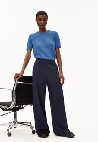 Avslappnad blå stickad tröja i kombination med navy vida byxor. Outfiten har en mjuk textur och kompletteras av en kontorsstol.