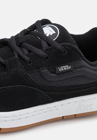 Gros plan d'une chaussure Vans noire avec tige en tissu et suède, lacets noirs, semelle intermédiaire blanche et semelle extérieure en gomme.
