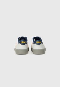 Baskets de skate blanches et marines avec des semelles grises, arborant une marque "LAKAI" jaune, des tiges en cuir lisse et des cols rembourrés.