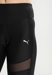 Czarne legginsy sportowe o prążkowanej fakturze, z przezroczystymi wstawkami z siateczki i białym logo Pumy z boku. Wysoki stan.