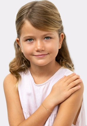 Gouden kettingarmband met een klein kruisje, gedragen om de pols van een kind met schouderlang haar, tegen een neutrale achtergrond.