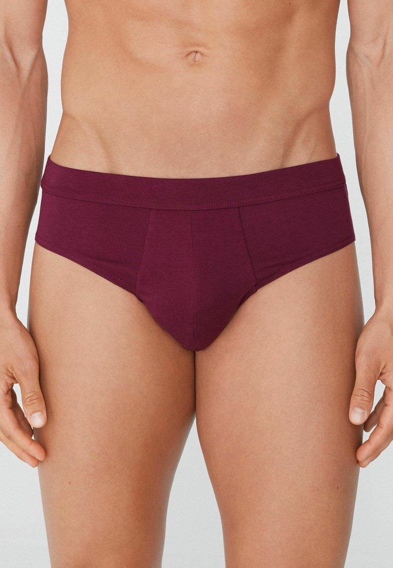 Burgundské pánské trenýrky vyrobené z měkké, elastické tkaniny. Mají široký pás a podpůrný design přední kapsy. Hladká textura, minimalistický styl.