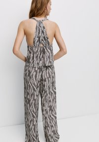 Grijze haltertop met een patroon en een open rug, met een vloeiende uitstraling, gecombineerd met bijpassende wijde broek met een soortgelijk patroon.