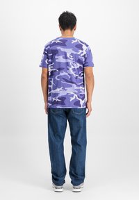 Lila kamuflažna majica iz bombaža, kratki rukavi, okrugli izrez, u kombinaciji s ležernim plavim trapericama i belim patikama.