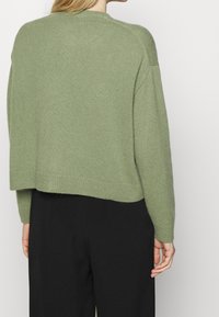 Zelený svetr z vlněné směsi s cropped designem, žebrovanými manžetami a lemem, který má texturovaný povrch. Zadní část je mírně delší než přední.