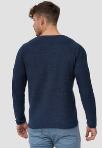 Navy sininen neulepusero, jossa on pitkät hihat, teksturoitu kangas, pyöreä pääntie, suora helma ja minimiyksityiskohtia takana.