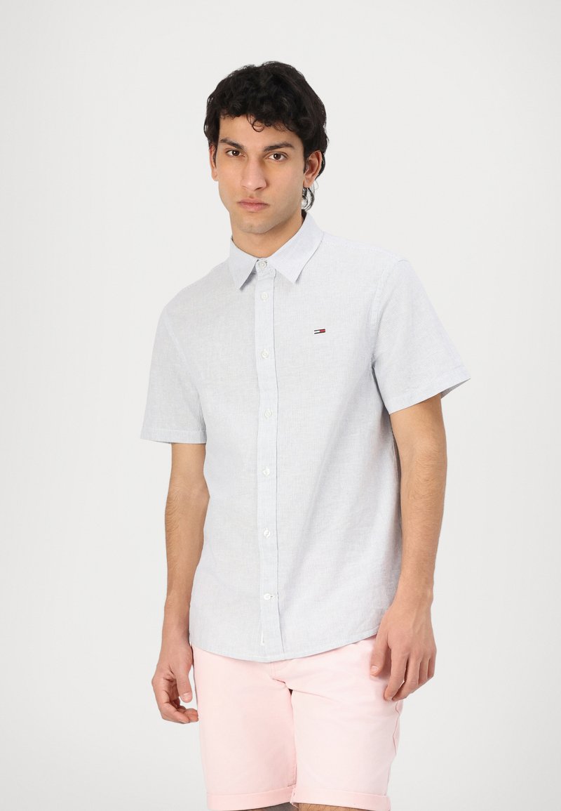 Kortermet knappskjorte i lys grå bomull med teksturert mønster og liten logo på venstre bryst. Stylet med rosa shorts.