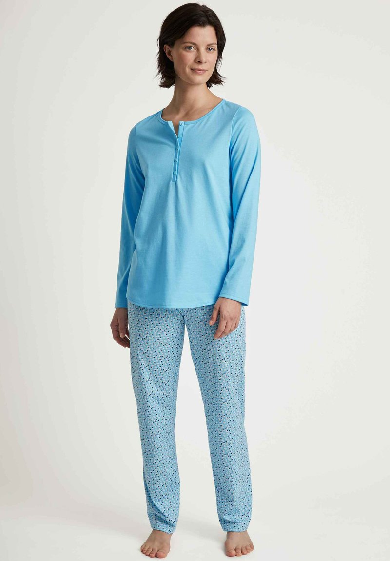 Lichtblauw pyjama overhemd met lange mouwen en knoopdetails, en bijpassende gestreepte broek met kleine bloemmotieven op een lichtblauwe achtergrond.