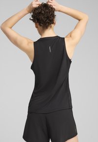 Top atletico senza maniche di colore nero, realizzato in tessuto leggero, con orlo curvo e piccolo dettaglio del logo sul retro. Abbinato a pantaloni corti neri.