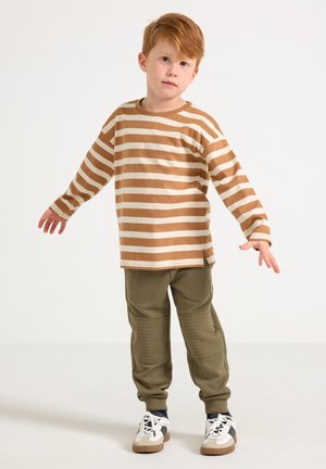 Brown and cream striped long-sleeve shirt paired with green jogger pants featuring textured knee panels and white sneakers with black accents.