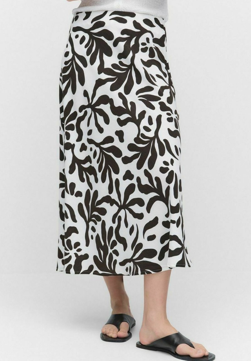 Jupe maxi en tissu blanc avec un bold motif de feuilles noires. Présente une taille haute et une forme évasée. Associée à des sandales en plastique noires.