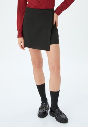 Musta kietaisuhame, jossa on vyölenkit ja sivutasku, suoramuotoinen. Yhdistetty mustiin loafer-kenkiin ja keskipitkiin mustiin sukkiin.