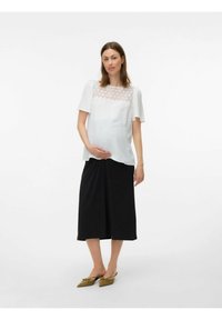 Vit topp med texturerad tyg och spetspanel, parat med en svart knälång kjol. Modellen bär olivgröna spetsiga ballerinaskor.