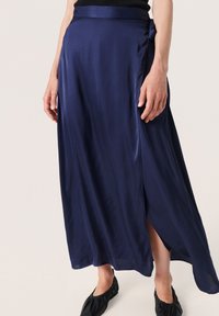 Navy blue satiinimaksihame, jossa on sivuhalkio, vyötäröllä solmukohta ja sileä, virtaava tekstuuri.