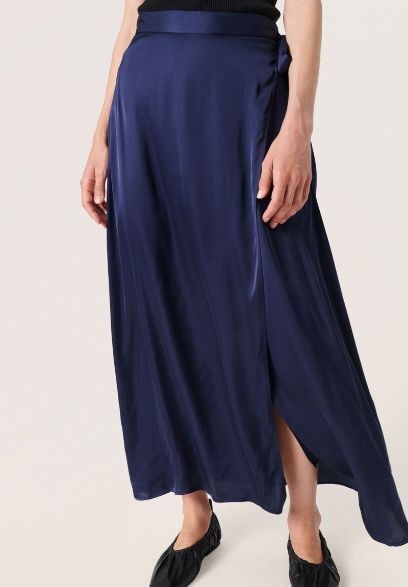 Navy blue satiinimaksihame, jossa on sivuhalkio, vyötäröllä solmukohta ja sileä, virtaava tekstuuri.