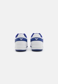 White sneakers with blue accents, featuring a textured design, padded collar, and rubber sole. Logo displayed on the heel.