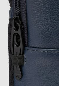 Marineblauwe leren tas close-up met een zwarte rits en gestructureerd materiaal, met zwarte accenten en stikseldetails.