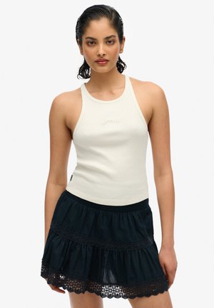 Kremowy T-shirt na ramiączkach z prążkowanej tkaniny o wysokim dekolcie, zestawiony z warstwową czarną spódnicą z koronkowym wykończeniem i elastyczną talią.