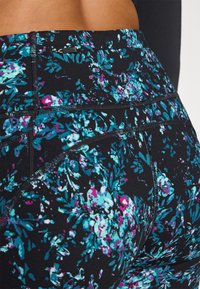 Fekete kompressziós leggings virágmintával, türkiz és magenta színekben, látható varrásokkal és elasztikus derékkal.