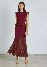 Vestido burdeos de canalé con mangas acampanadas rizadas y cintura peplum, con una falda plisada que fluye hasta los tobillos. Sandalias de tacón transparente.