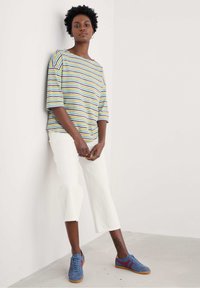 Top ligero a rayas en colores pastel con cuello barco, combinado con pantalones blancos cortos y zapatos deportivos azules con acentos rojos.