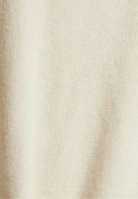 Gros plan d’un tissu tricoté beige montrant des points fins et réguliers ainsi qu’une texture douce avec une ombrage subtile.