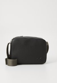 Black textured leather crossbody bag with a rectangular shape, featuring a zip closure and olive green strap. Logo embossed on side.