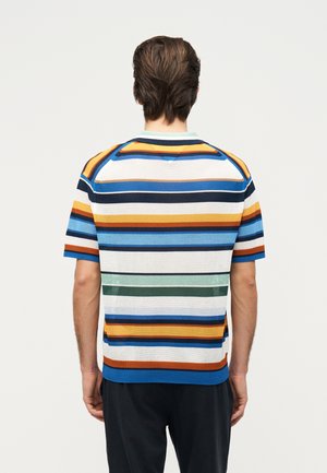 Mand iført en kortærmet strikket trøje med vandrette striber i blå, hvid, orange, brun og grøn, vendt væk fra kameraet.