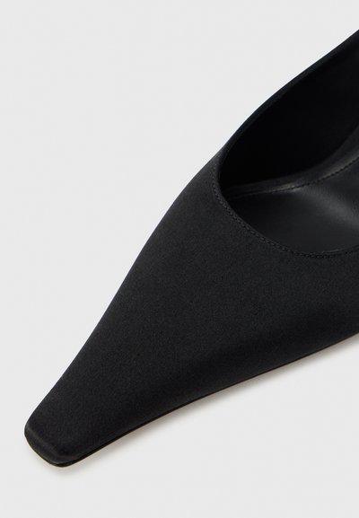 Μαύρο παπούτσι με μυτερή μύτη, εξωτερικό από λείο ύφασμα, ανοιχτές πλευρές και χαμηλό τακούνι. Η εσωτερική επένδυση είναι από μαύρο δέρμα, δημιουργώντας έναν κομψό σχεδιασμό.