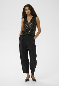 Zwarte pailletten top met een V-hals, gecombineerd met hoge zwarte broeken en zwarte flats. Gladde textuur en iets taps toelopende fit.