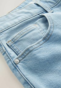 Jeans din denim de un albastru deschis, având o buzunar vizibil, cusături contrastante și un detaliu cu un buton argintiu pe talie.