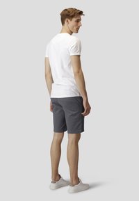 Hvit t-skjorte med korte ermer og grå shorts, laget av mykt stoff med en tettsittende design. Modellen står med ryggen til kameraet, iført hvite joggesko.