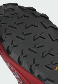 Semelle extérieure noire robuste avec des crampons triangulaires profonds et une semelle intermédiaire rouge, conçue pour une meilleure adhérence et une utilisation en extérieur.