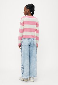 Maglioncino a righe rosa e beige con un design cropped, abbinato a pantaloni cargo larghi di colore azzurro chiaro e dotati di molte tasche.