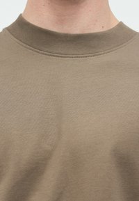 Μπλούζα σε χακί χρώμα με στρογγυλή λαιμόκοψη. Κατασκευασμένη από απαλό, λείο ύφασμα με ελαφριά λάμψη και ελάχιστες ραφές.