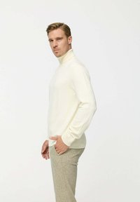 Krém színű garbós pulóver hosszú ujjal, testhezálló fazonban, puha anyagból készült, világosszürke, texturált nadrággal párosítva.