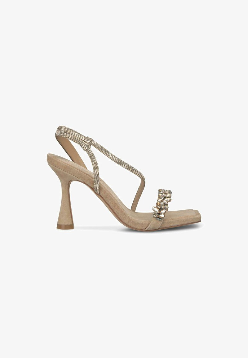 Beige suède slingback-hakje met een glinsterende band en een decoratieve metalen accent aan de voorkant. Glad textuur en minimalistisch ontwerp.