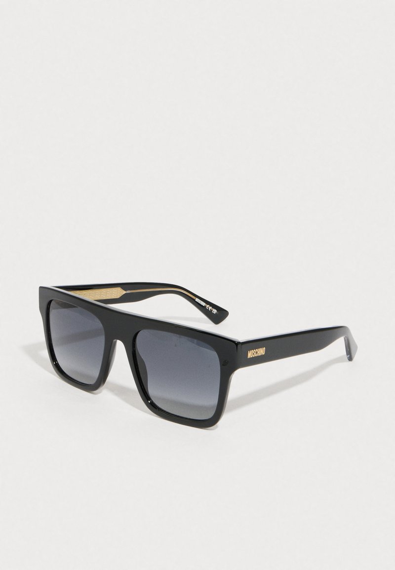 Óculos de sol pretos com uma armação quadrada ousada e lentes cinzentas em gradiente. As hastes apresentam detalhes em dourado e identificação da marca.