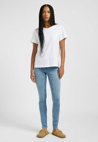 Camiseta blanca de algodón de manga corta, combinada con jeans slim fit de color azul claro y calzado sin cordones de color beige. Diseño sencillo y ajuste casual.