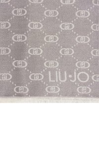 Szary materiał z powtarzającym się wzorem logo, z jasnymi teksturowanymi akcentami i frędzlami na brzegach. Wyróżniająca się nazwa "LIU-JO".