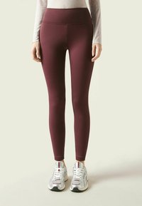 Leggings burdeos de tiro alto con una textura suave y elástica, combinados con zapatillas deportivas plateadas con detalles de malla y cordones.