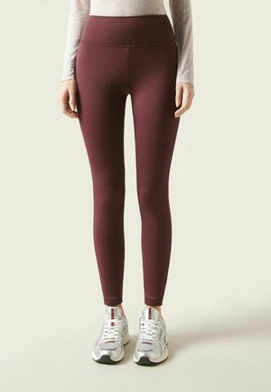 Bordeaux højtaljede leggings med en glat, strækbar tekstur, parret med sølvfarvede sportsko med mesh-detaljer og snørebånd.