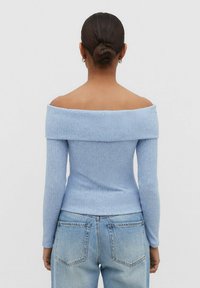 Hellblaues, schulterfreies Rippoberteil mit langen Ärmeln, figurbetontem Schnitt und weicher Textur, kombiniert mit abgetragenen blauen Jeans.