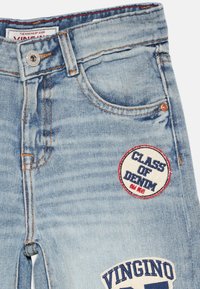 Světle modré džíny z denimu mají měkkou strukturu, knoflíky a dva nášivky: "CLASS OF DENIM" a "VINGINO" s kontrastními barvami a prošíváním.