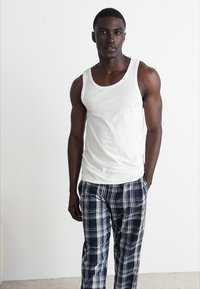 Camiseta sin mangas blanca y pantalones de pijama de cuadro azul. El tejido parece ligero. Los pantalones presentan un patrón de cuadros en azul marino, blanco y azul claro.