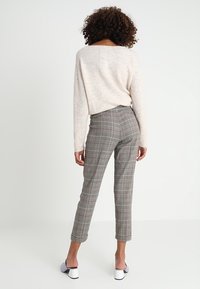 Un pull en tricot beige clair associé à un pantalon à carreaux gris. Le pantalon présente une coupe ajustée et une longueur raccourcie, avec de subtils accents rouges.