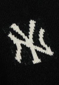 Μαύρο πλεκτό ύφασμα με ένα έντονο λευκό γραφικό σχέδιο που μοιάζει με τα γράμματα "NY" ή ένα παρόμοιο αφηρημένο μοτίβο.