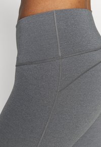 Leggings de talle alto gris con una textura suave y elástica. Presentan costuras planas y un diseño elegante, adecuado para actividades atléticas.