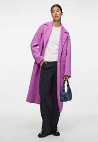 Roosa villane mantel laienevate kraede ja küljetaskutega, kantakse valge pluusi kohal. Mustad triibulised püksid ja väike sinine mustriga kott.